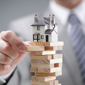 A man in a suit holding wooden blocks with a house on top, representing a surplus funds claim. - Dubyak Law Firm, P.A.